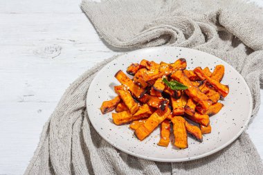 Baharatlı ve soslu fırında organik batata kızartması. Tatlı sebze, porsiyon ve çatal bıçak takımı hazır vejetaryen yemeği. Beyaz alçı arkaplan, kopyalama alanı