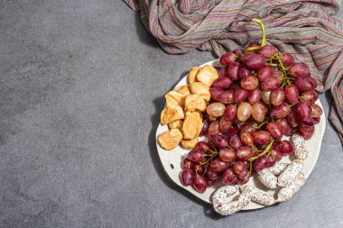 Peynirli abur cubur tabağı, üzüm ve kurutulmuş sosis. Şarküteri antipasto, taş beton arka plan. Modaya uygun sert ışık, koyu gölge, düz uzanma, üst manzara