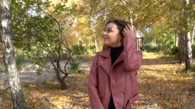 Sonbahar parkında pembe deri ceketli esmer bir kadın.