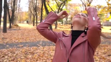 Sonbahar parkında pembe deri ceketli esmer bir kadın.