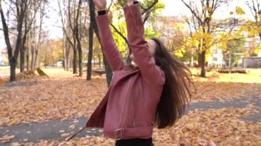 Sonbahar parkında genç bir kadın kuru yapraklar döker, mutlu kız.