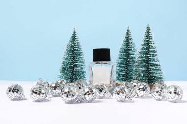 Damgasız parfüm şişesi, gümüş noel baloları ve mavi arka planda köknar ağaçları. Boşluğu kopyala