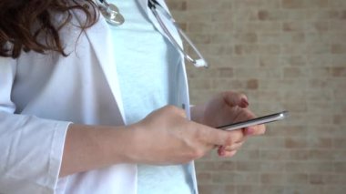 Beyaz önlük giyen kadın doktor, uzaktan hastaya mesaj gönderen akıllı telefon uygulamaları kullanıyor.