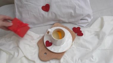Breakfast in bed, cup of green tea with hearts, hand puts a gift . Valentine's day or Women's day concept