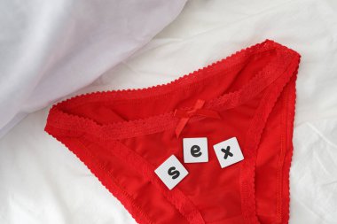 Seks konsepti, kırmızı dantelli külot, beyaz yataktaki tahta harflerden kelime seksi. Romantik gece, kadın iç çamaşırı