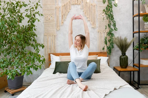 stock image Photo of young happy woman stretching her arms and smiling while sitting on bed