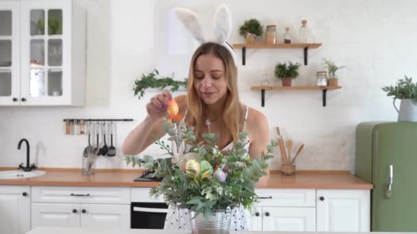 台所で花束を飾るウサギの耳を身に着けている美しい女性 ハッピーイースター — ストック動画