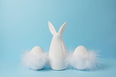 Mavi arka planda tüyleri olan Paskalya tavşanı ve yumurta, tebrik kartı.