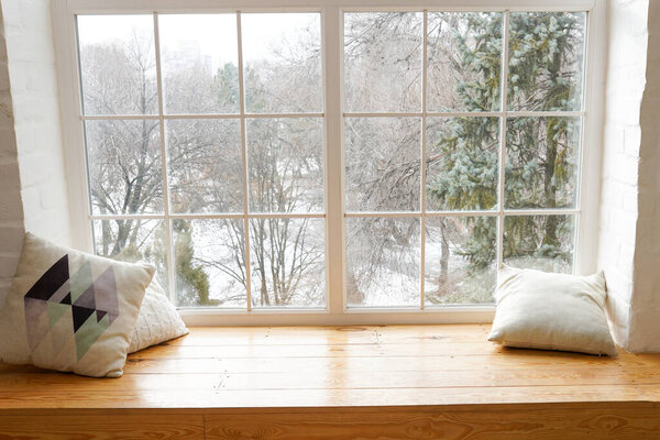 ?ozy and frost winter still life, white pillows on windowsill against snow landscape from outside