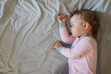 Gri arka planda uyurken bir yatakta uzanan huzur dolu bir bebek.