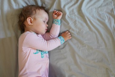 Gri arka planda uyurken bir yatakta uzanan huzur dolu bir bebek.