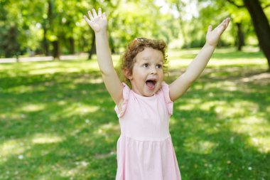 Küçük, çekici, pembe elbiseli neşeli bir kızın portresi. Eğlenin ve parkta yürüyün.