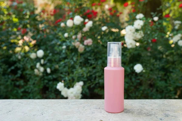 Pink cosmetic bottle with hand, face, body cream on green nature background with flowers. Beauty skin care product, template