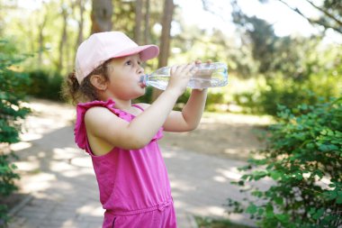 Çocuk parktaki bir şişeden maden suyu içiyor.