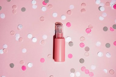 Pembe renkli konfeti ve pembe arka planda gölgesi olan pembe bir kozmetik şişesi. Güzellik spası tıbbi cilt bakımı ve kozmetik krem ambalaj ürünleri.