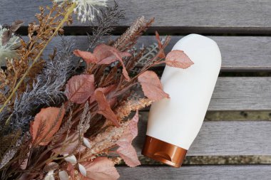 Kozmetik beyaz şişe, sarı sonbahar çiçekleri ve tahtada yapraklar. Organik doğal kozmetik kavramı. Düzleştirici. Tasarım mozaiği