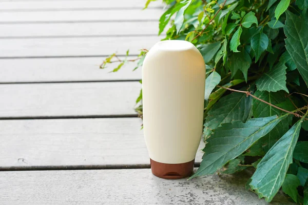 White bottle with shampoo or lotion staying on the wood with green leaves background