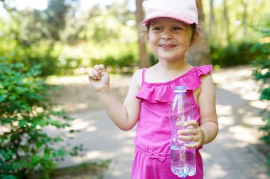 Child girl in pink cap holding mineral water bottle in the green park