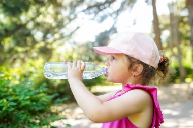 Çocuk parktaki bir şişeden maden suyu içiyor.
