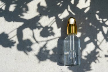 Dropper glass Bottle Mock-Up with leaves shadows on concrete background. Body treatment and spa. Natural beauty products. Eco cream, serum, skin care blank bottle. Anti-cellulite massage oil