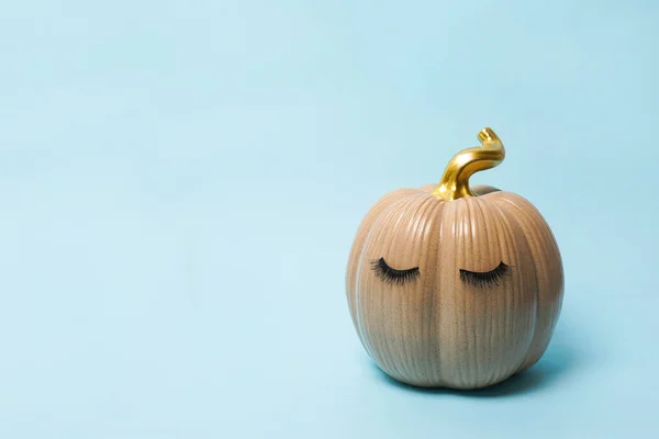 Pumpkin with false eyelashes on blue background. Autumn, fall, halloween concept. copy space