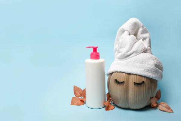 mock up cosmetic spray bottle and pumpkin with towel and false eyelashes on blue background with autumn leaves, hair and facial skin care in autumn