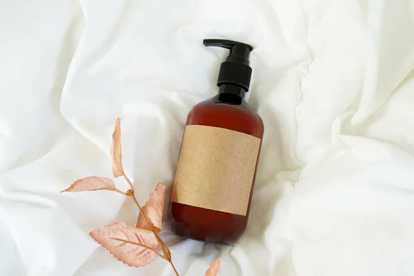 Brown pump cosmetic bottle with autumn leaves on white bed background. Cosmetic packaging mockup. Flat lay, top view