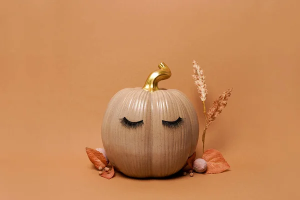 Pumpkin with false eyelashes and autumn leaves on orange background. Autumn, fall, halloween concept. copy space