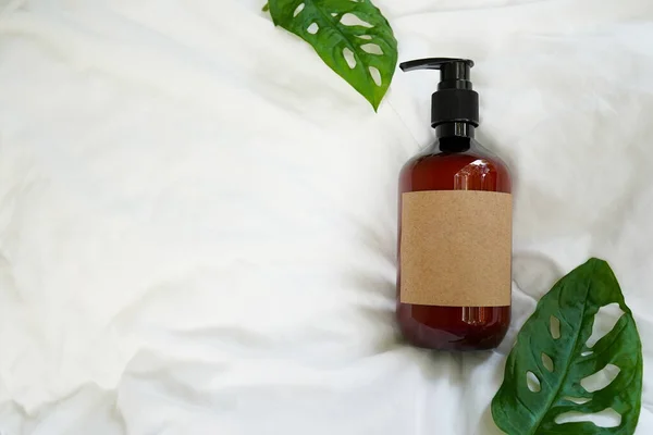 Spray in brown cosmetic bottle with monstera leaves on white bed background. DIY room spray with herbal essential oils. top view, copy space