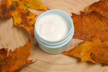 Cosmetic cream with autumn falling leaves on wooden background