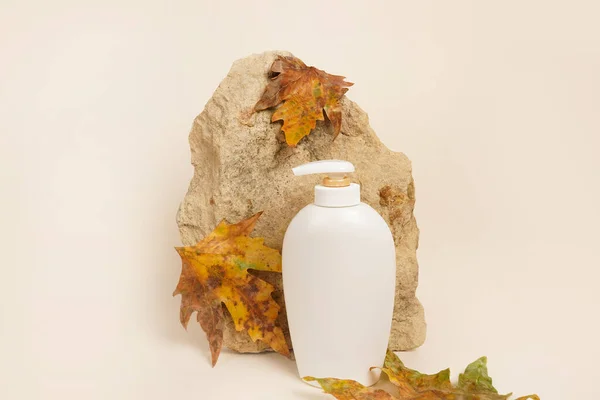 Soap or lotion bottle, brick and dry autumn leaves on light background, creative still life cosmetic photography
