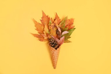 Ice cream cone with autumn leaves on light background, copy space, flat lay. Colorful bright creative layout