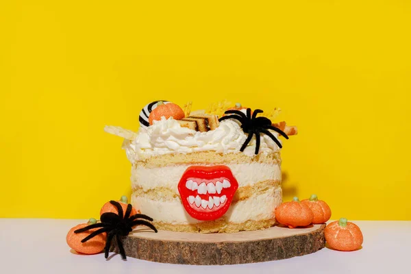 Halloween white cake with pumpkins, spiders and lips staying on the wood on yellow background, copy space