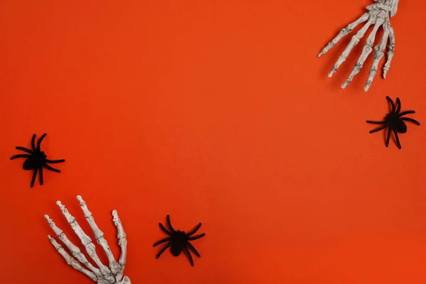 Halloween frame with skeleton hands and spiders, red background. Halloween concept. Flat lay, top view, copy space