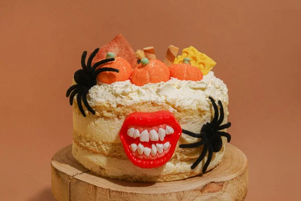 Halloween white cake with pumpkins, spiders and lips staying on the wood on orange background