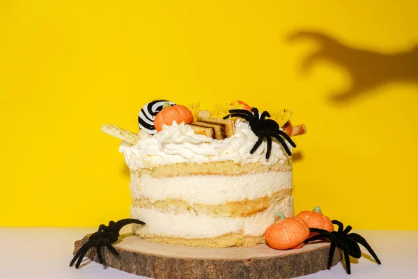 Halloween cake with pumpkins, spiders and shadow of the hand on yellow background