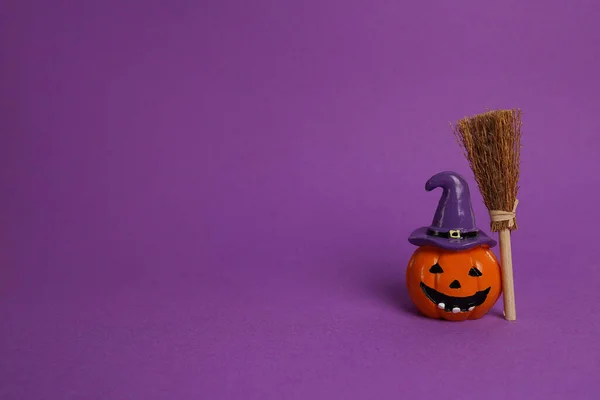 Halloween pumpkin jack o lantern decor with funny face and witch broom on purple background, copy space