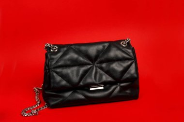 Kırmızı zincire vurulmuş siyah bir kadın çantası.