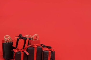 Siyah kağıt alışveriş torbaları ve kırmızı arka planda küçük hediye kutuları, kopyalama alanı. Kara Cuma konsepti