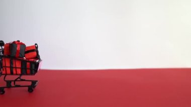 Kırmızı ve beyaz arka planda alışveriş arabasında siyah hediye kutuları. Kara Cuma