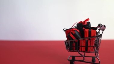 Kırmızı ve beyaz arka planda alışveriş arabasında hediye kutuları. Kara Cuma