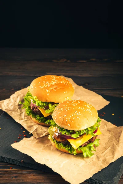 Tasty hamburgers on wooden board on dark background.