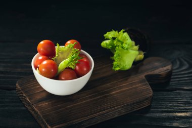 koyu ahşap arka plan üzerinde bir kase ve kiraz domates marul yaprakları