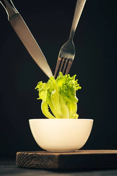 Koyu arkaplanda çatallı ve bıçaklı yeşil salata