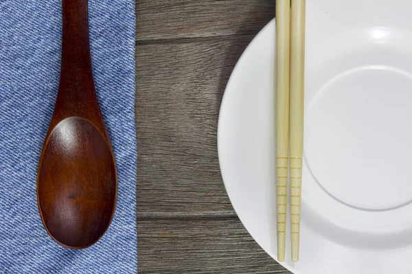 Wood background plates, chopsticks and spoons on blue jeans text — Stock Photo, Image