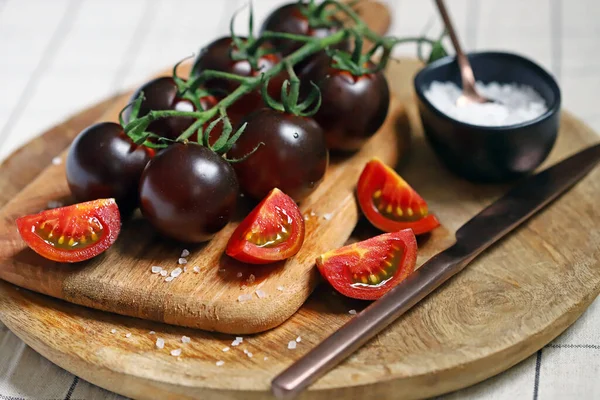 Black tomatoes on a twig on a wooden board. Pieces of black tomatoes with sea salt.