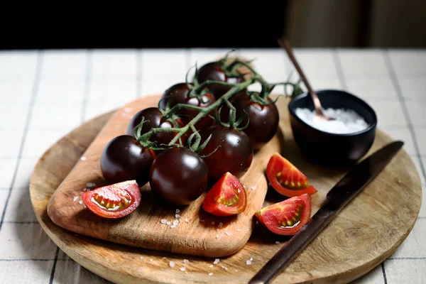 Black tomatoes on a branch on a wooden board with sea salt.