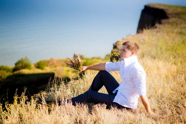 Guy with flowers sitting on a cliff