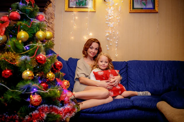 Mother and daughter sitting on the sofa near the Christmas tree