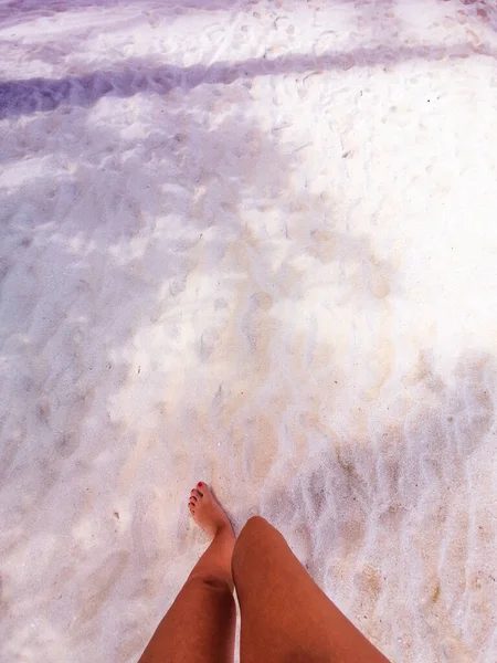 Feet of woman with colored nails trample the white beach of Maldives.